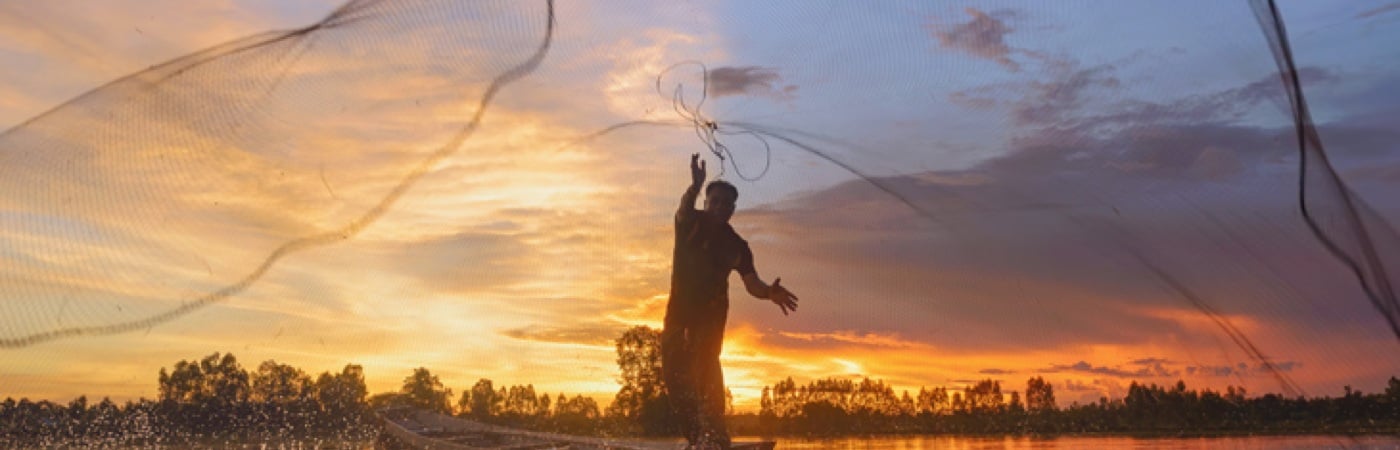 Man throwing fishing net at sunset