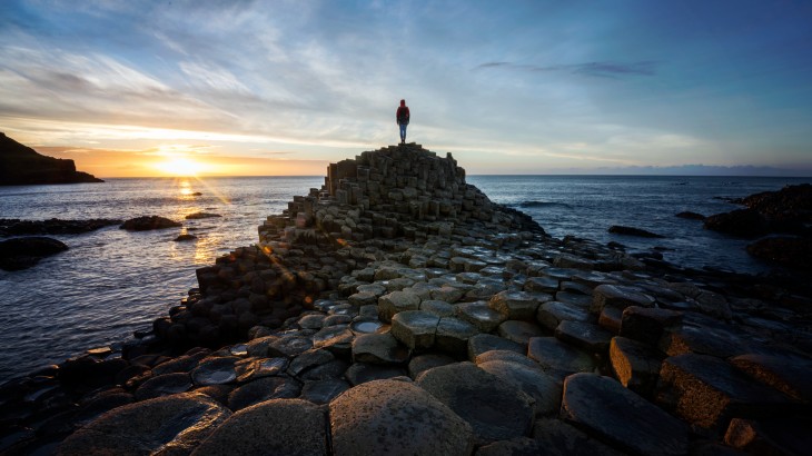 Woman standing on Giants Causeway at sunset